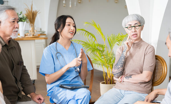 A young care professional talking to Asian elders