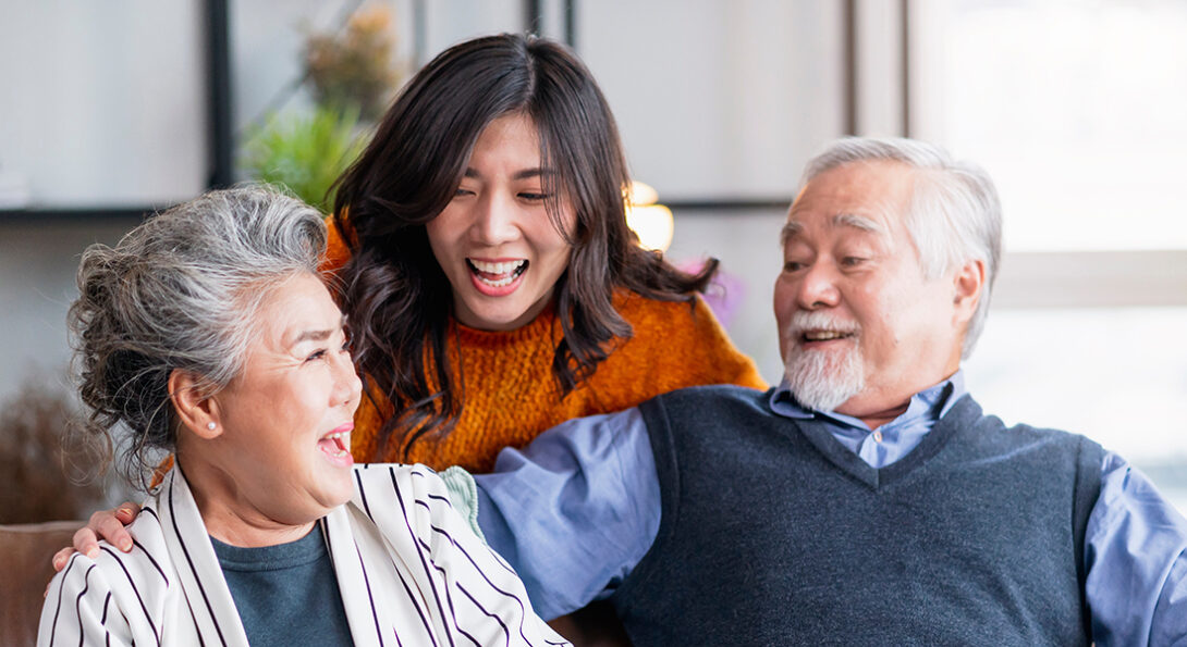An elderly Asian American couple sitting with a younger Asian American woman standing behind them